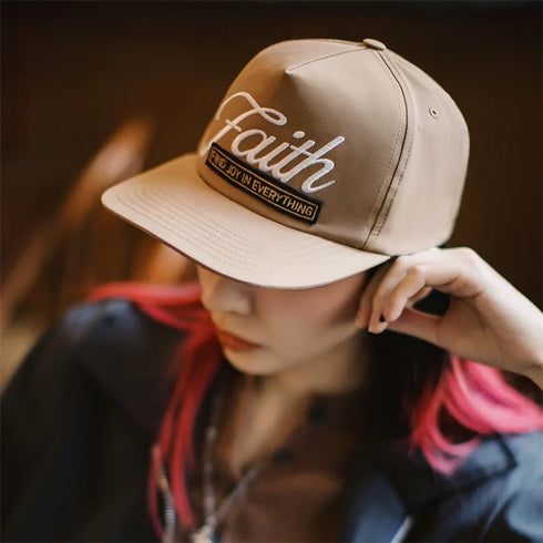 Person wearing a beige cap with 'Faith' text, blurred background